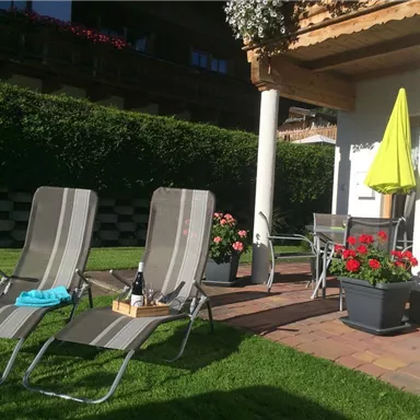 A cozy garden area with two lounge chairs and a sun umbrella. Colorful flowers and a small sitting area create an inviting atmosphere.
