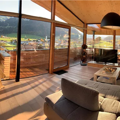 A modern living room with large windows and a view of the mountains. The furniture is comfortable and stylishly arranged.
