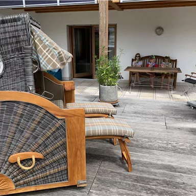 A cozy terrace with a sun lounger and a dining table in the background. Potted plants add an inviting atmosphere to the space.