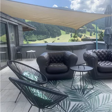 An elegant terrace with modern furniture and a view of a green landscape. The atmosphere is inviting and relaxed, perfect for sunny days.