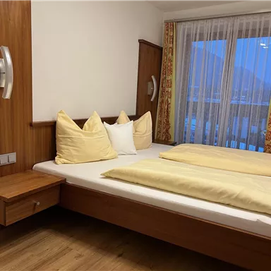 Ein gemütliches Schlafzimmer mit einem Doppelbett, Holzvertäfelung und großen Fenstern. Die Kissen und Decken sind in sanften Farben gehalten.