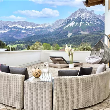 Eine moderne Terrasse mit bequemen Sitzmöbeln und Blick auf beeindruckende Berge. Die Umgebung ist hell und einladend, ideal zum Entspannen.