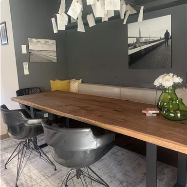 A modern dining area with a large wooden table and black chairs. Pictures and notes hang on the wall, creating a cozy atmosphere.