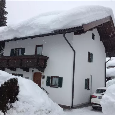 Ein Haus im Schnee mit einem hohen Schneedecken auf dem Dach. Die Umgebung ist winterlich und es gibt viel Schnee.