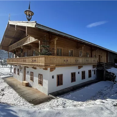 Ein wunderschönes Holzgebäude im Alpenstil, umgeben von Schnee. Der klare blaue Himmel und die Berge im Hintergrund verleihen der Szene einen malerischen Charme.