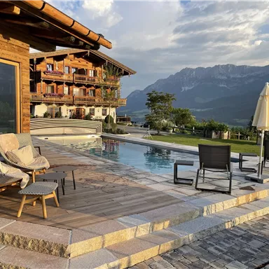A luxurious terrace with a pool and comfortable seating options. In the background, majestic mountains and a picturesque landscape can be seen.