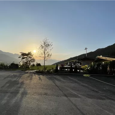 A picturesque landscape at sunset with mountains in the background. In the foreground, an empty road and some trees.