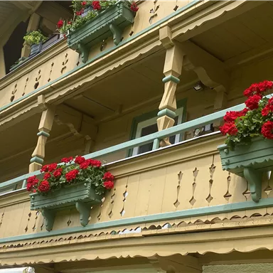 A traditional wooden building with a balcony adorned with red geraniums. The architecture features a detailed facade design and presents an inviting impression.