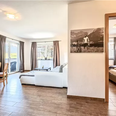 Ein helles und geräumiges Wohnzimmer mit Holzfußboden. Es gibt eine gemütliche Sitzecke, einen Essbereich und einen Blick auf die Berge.