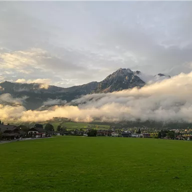 A picturesque landscape with green meadows and majestic mountains. Gentle clouds wrap around the peaks under a clear sky.