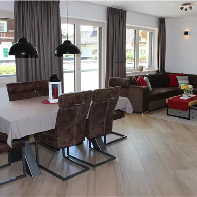 A modern and inviting living kitchen with a dining table and comfortable seating. Large windows let in plenty of daylight and create a bright atmosphere.