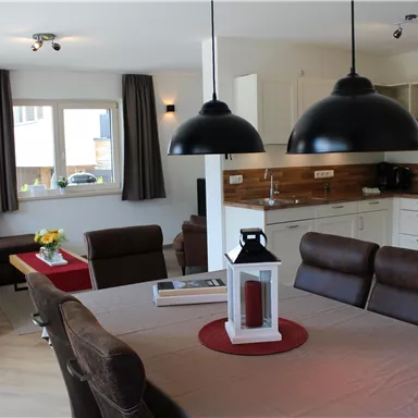 A modern living room with an open kitchen. The space is bright and inviting, with a dining table and cozy seating.