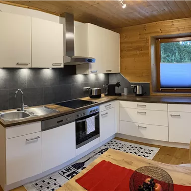 Eine moderne Küche mit weißen Schränken und Holzdekor. Sie ist gut ausgestattet mit Geräten und großen Fenstern. Über die Balkontür kommt man auch auf die Terrasse.