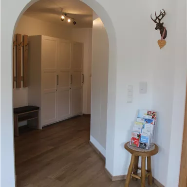 A bright entrance area with an arched passage. On the right side, there is a small table with brochures and on the left are white cabinets.