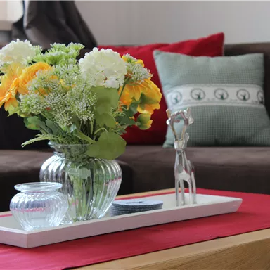 A stylishly decorated table with a flower vase and a small decorative object. In the background, a cozy sofa and cushions can be seen.