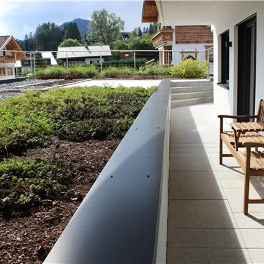 A beautiful balcony with a wooden bench and a view of a green landscape. In the background, houses and mountains can be seen.