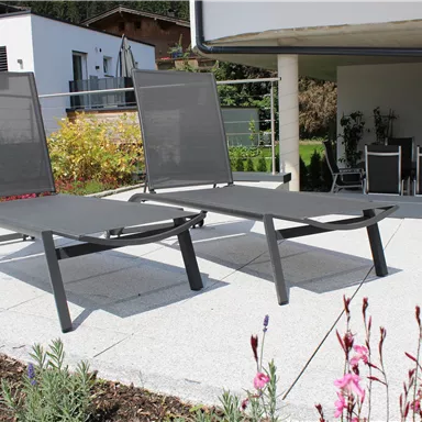 Two modern loungers on a terrace. In the background, plants and a cozy seating area are visible.