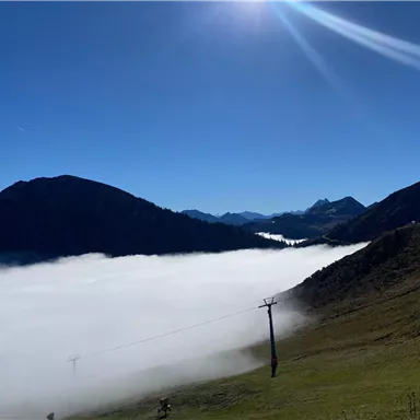 A picturesque mountain landscape with low-hanging clouds in the valley. The sky is clear and sunny, highlighting the beauty of nature.