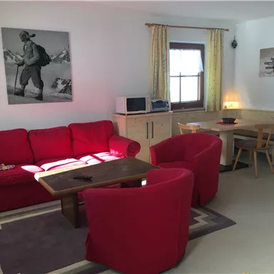 A cozy living room with a red sofa and chairs. There is a table and some pictures on the walls.