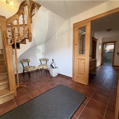 An inviting hallway with a wooden staircase and cozy furnishings. A large carpet and tiled floor give the room warmth and comfort.