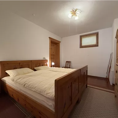 A cozy bedroom with a large wooden bed and two pillows. The walls are light, and there is a closet as well as a small bedside table.