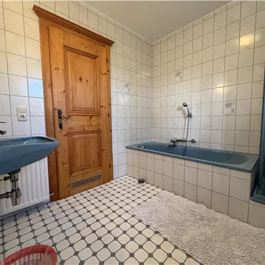 A bathroom with white tiles and blue fixtures. There is a bathtub, a shower, and a wooden door.