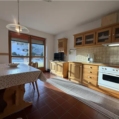 A bright kitchen with wooden cabinets and a large table. A window offers a view of the garden.