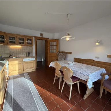 A cozy kitchen with wooden shelves and a dining table. The decor is simple and inviting with plenty of space for cooking and eating.