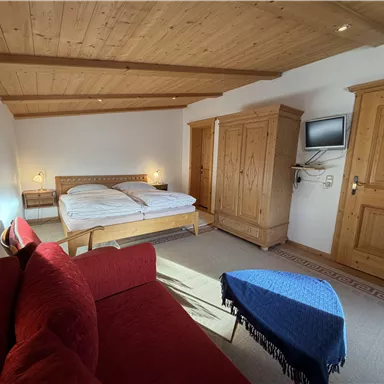 A cozy bedroom with a double bed and a red sofa. The room has wooden furniture and a television on the wall.