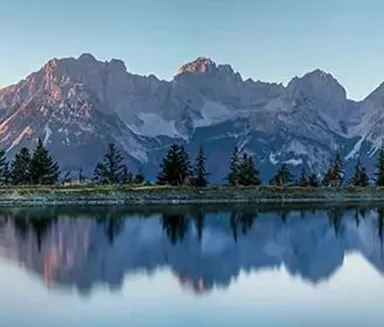A majestic mountain landscape is reflected in a tranquil lake. The colors of the sunrise illuminate the peaks and create a peaceful atmosphere.