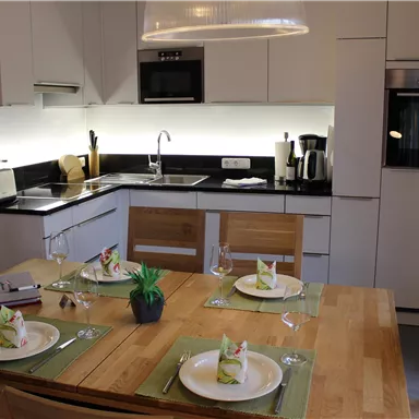 A modern kitchen unit with minimalist designs and bright lighting. The dining table is beautifully set with plates and fresh napkins.