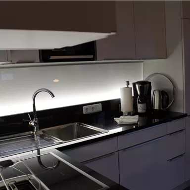 A modern kitchen with black countertops and white cabinets. There is a faucet, kitchen appliances, and elegant lighting.