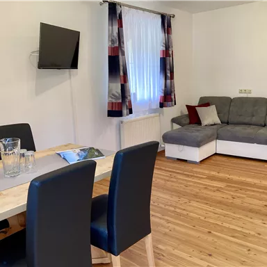 Eine gemütliche Wohnung mit einem Essbereich und einem Wohnzimmer. Der Raum hat eine helle Atmosphäre mit einem Sofa und einem Fernseher.