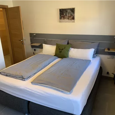 A cozy bedroom with a large double bed and modern furniture. A picture hangs on the wall and there are windows with curtains.