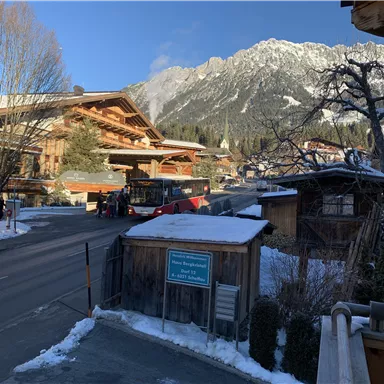 A snow-covered mountain landscape with traditional wooden houses. A bus is stopping on the road in front of the mountains.
