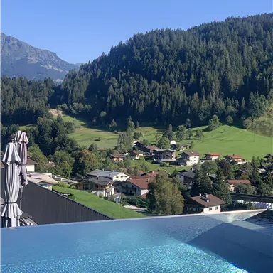 A beautiful view of a pool with clear water, surrounded by green mountains and forests. In the foreground, you can see a quiet village with houses and trees.