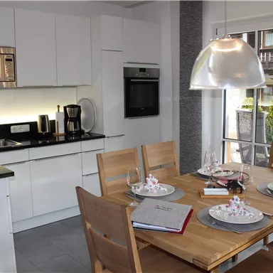 A modern kitchen with a wooden dining group and elegant dishes. The white cabinets and the black countertop give a stylish look.