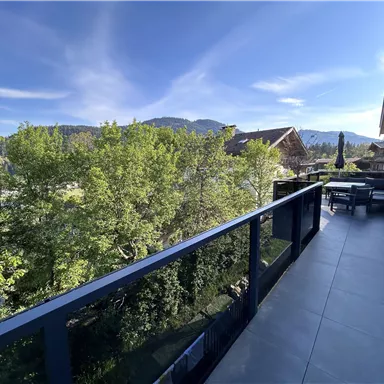 Ein Balkon mit Blick auf Bäume und Berge. Der Himmel ist klar und strahlend blau.