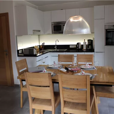 A modern kitchen with a wooden dining area. The room is bright and inviting, with kitchen appliances and a large window.