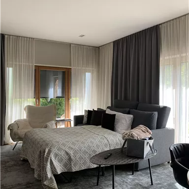 A modern bedroom with a cozy bed and stylish furniture. Large windows let in plenty of daylight and create a bright atmosphere.
