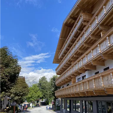A modern building with wooden balustrades and a clear blue sky. The road runs through a picturesque landscape with trees and guests.