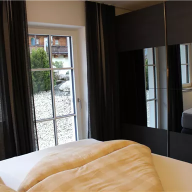 A modern furnished bedroom with large windows and a wardrobe. The room has bright colors and feels inviting.