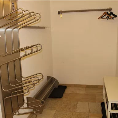 An empty room with a clothes rack and a hook. The walls are white, and the floor is made of tiles.