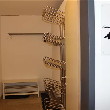 A simple room with a clothing rack and a bench. On the wall hangs a sign with a mountain motif.