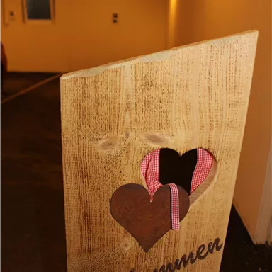 A wooden sign with the inscription "Welcome" and heart cutouts. In the background, a well-lit parking lot is visible.