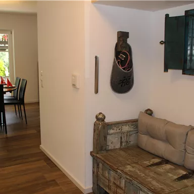 An inviting hallway with an old wooden sofa and a decorative mirror. In the background, a dining area with a table and chairs is visible.
