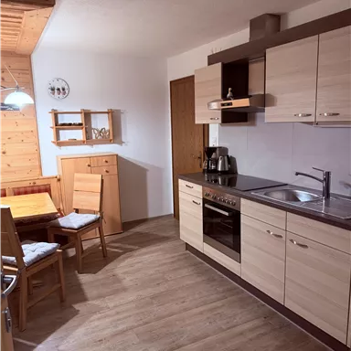 A modern kitchen with light wooden cabinets and a cozy dining table corner. The equipment includes a stove, a sink, and a coffee machine.
