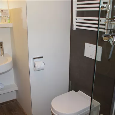 A modern bathroom with a shower, a sink, and a toilet. The walls are bright and clean, and there is a towel rack.