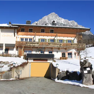 A picturesque building with several balconies, surrounded by snow-covered landscapes. In the background, a high mountain rises under a clear blue sky.