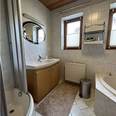 Ein helles Bad mit einer Dusche, einer Badewanne und einem Waschbecken. Große Fenster sorgen für ausreichend Tageslicht.